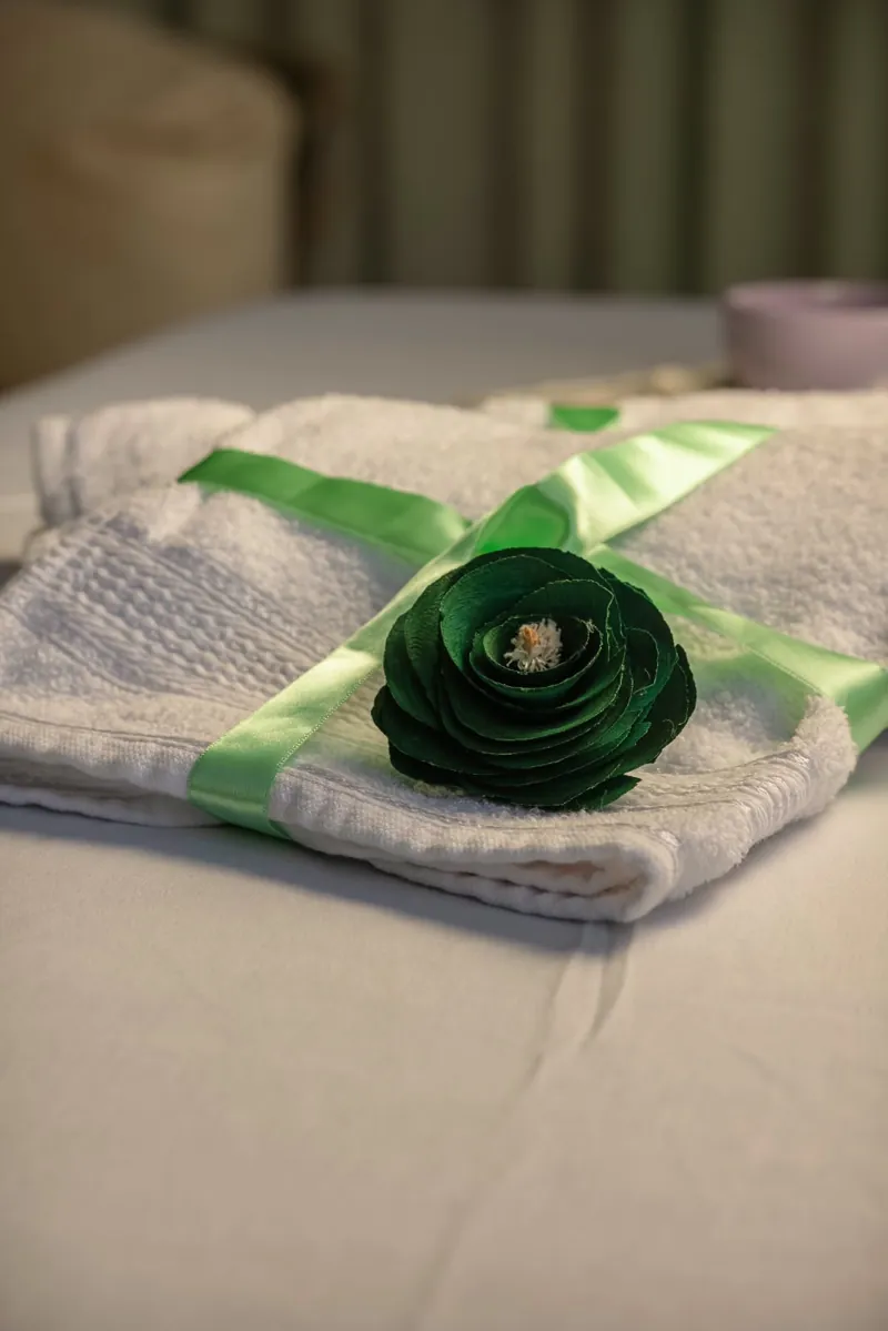 Toalhas brancas com laço verde e flor decorativa sobre a maca